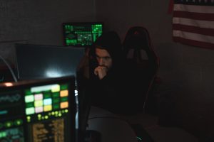 Security Researcher sits in dark room in front of a RGB keyboard surrounded by monitors