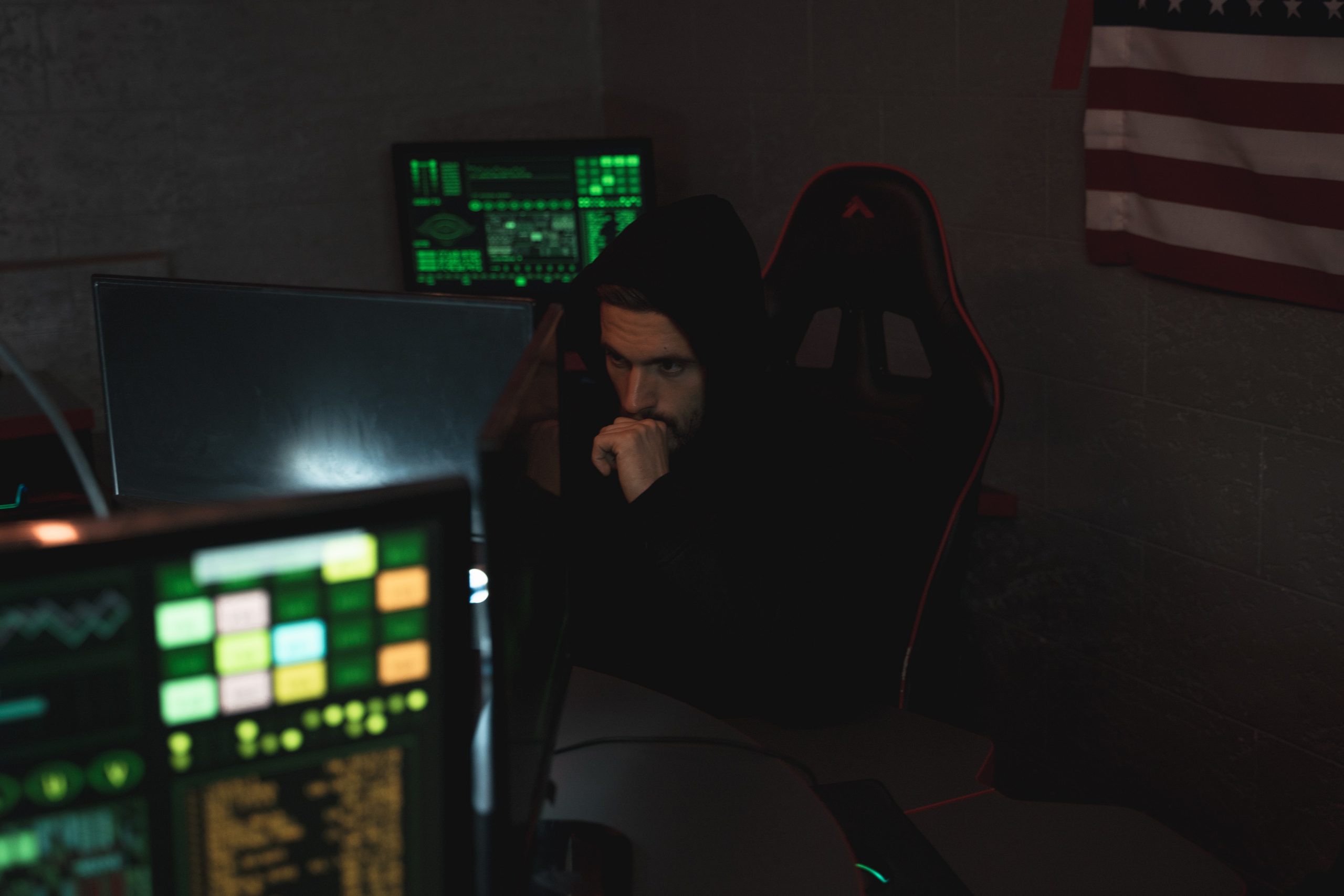 Security Researcher sits in dark room in front of a RGB keyboard surrounded by monitors